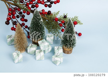 Composition with colorful gifts, a branch of holly with its red berries and christmas tree against a luminous sky-blue background. Composition with colorful gifts, a branch of holly with its red berries and christmas tree against a luminous sky-blue background. 108120279