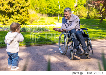Dad on wheelchair playing with his little son in the park 108121954