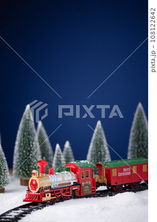 Toy locomotive on railway in the snow with Christmas tree. Christmas and New Year background. Creative winter Christmas composition. 108122642