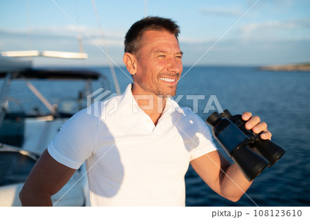 Smiling man in white with binocular standing on the yacht 108123610