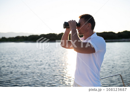 Man with binocular standing on a yacht deck Man with binocular standing on a yacht deck 108123687
