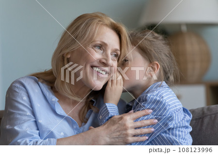 Cute little kid girl telling secret to cheerful mature grandma Cute little kid girl telling secret to cheerful mature grandma 108123996