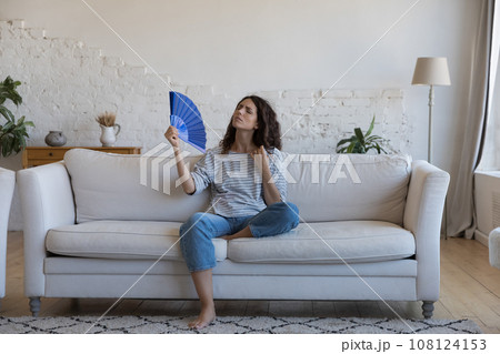 Exhausted frustrated Hispanic woman waving paper handheld fan 108124153