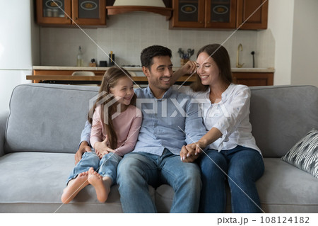 Happy joyful attractive parents and kid girl resting on sofa Happy joyful attractive parents and kid girl resting on sofa 108124182