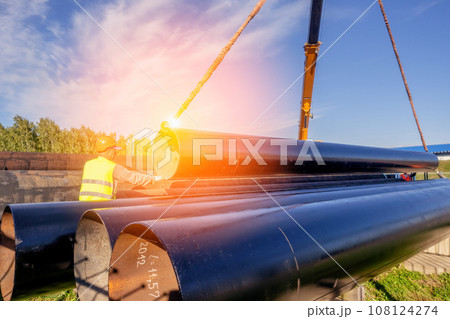 Slinger unloads large gasification pipes on summer day. Pipes for transporting natural gas Slinger unloads large gasification pipes on summer day. Pipes for transporting natural gas 108124274