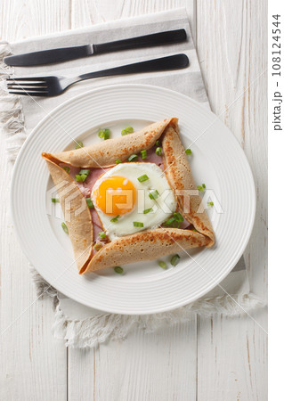 Homemade buckwheat crepe galette with egg, ham and green onion closeup on the plate. Vertical top view Homemade buckwheat crepe galette with egg, ham and green onion closeup on the plate. Vertical top view 108124544