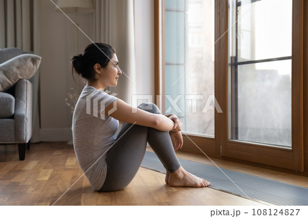 Dreamy Indian woman looking out window, sitting on floor Dreamy Indian woman looking out window, sitting on floor 108124827
