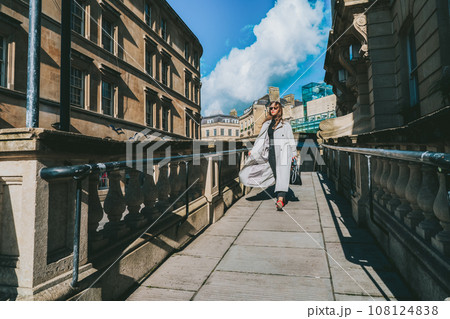 Outdoor autumn portrait of young elegant fashionable woman wearing trendy sunglasses, gray color coat, black jeans and turtleneck walking on street of European city in sunny day. street style fashion. 108124838