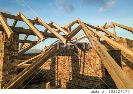 Private residential house with wooden roof frame structure under construction. Unfinished brick building under development. 108127179