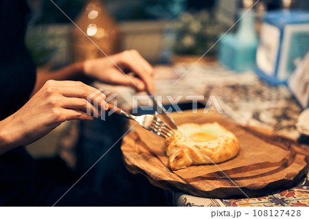 Women's hands cut baked bread with cheese and egg filling with a knife. Khachapuri in Adjarian is a traditional dish of Georgian cuisine. High quality photo 108127428