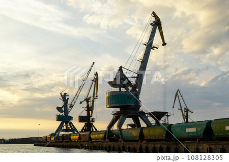 Harbor cranes with grain wagons between crane legs, seaport industry scene, grain export 108128305