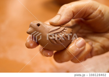 Unrecognizable potter master holding bird sculpture from clay clay in hand. Unrecognizable potter master holding bird sculpture from clay clay in hand. 108128402
