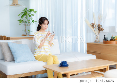 部屋でスマホを操作する若い女性 108128673