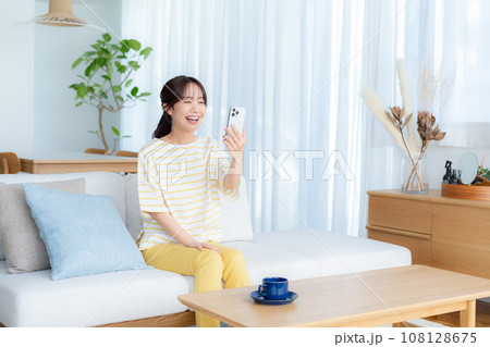 部屋でスマホを操作する若い女性 108128675