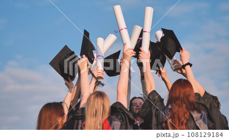 Graduates connect diplomas and caps on a sunny day. 108129184