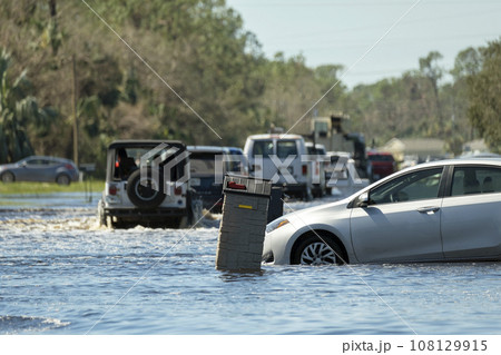 Flooded Florida road with evacuating cars and surrounded with water houses in suburban residential area. Consequences of hurricane natural disaster 108129915