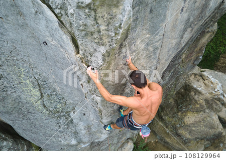 Determined climber clambering up steep wall of rocky mountain. Sportsman overcoming difficult route. Engaging in extreme sports and rock climbing hobby concept. 108129964