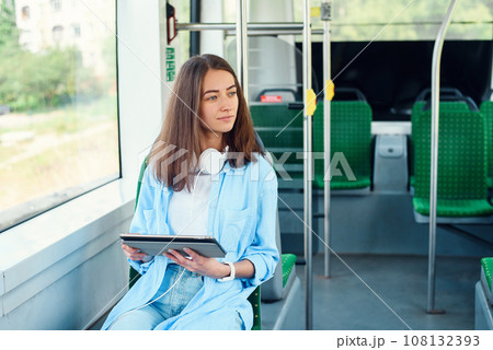 Happy smiling woman reads a tablet or ebook in a modern tram or subway. Pretty girl rides for work in public transport. 108132393