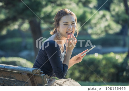 公園のベンチでスマホを見る若い女性 公園のベンチでスマホを見る若い女性 108136446