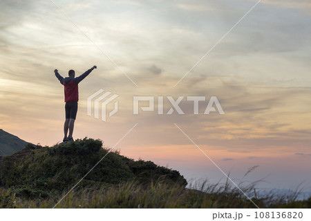 Dark silhouette of a hiker climbing a mountain at sunset raising his hands standing on summit like a winner. Dark silhouette of a hiker climbing a mountain at sunset raising his hands standing on summit like a winner. 108136820