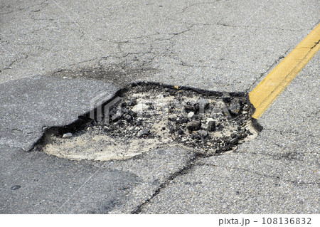 Damaged asphalt road with deep pothole on american highway surface. Ruined roadway in urgent need of repair Damaged asphalt road with deep pothole on american highway surface. Ruined roadway in urgent need of repair 108136832