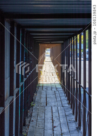 An improvised visual tunnel made of a metal fence along the roadway with wooden flooring. An improvised visual tunnel made of a metal fence along the roadway with wooden flooring. 108139843