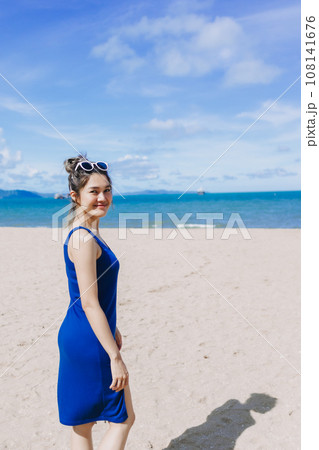 Vertical portrait of happy woman in. blue dress walking on the beach. Vertical portrait of happy woman in. blue dress walking on the beach. 108141676