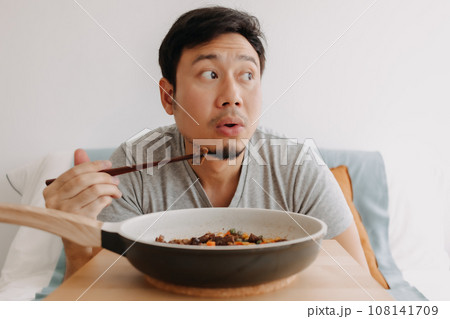 Happy funny face of man eating homemade food in the pan with chopsticks. 108141709
