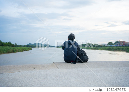asian man sit and relax at side of river during sunset 108147678