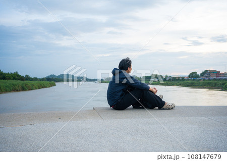 asian man sit and relax at side of river during sunset 108147679