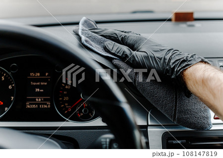 Man's hand in black glove cleaning car interior, dashboard and leather seats with microfiber cloth 108147819