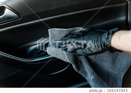 Man's hand in black glove cleaning car interior, dashboard and leather seats with microfiber cloth 108147843