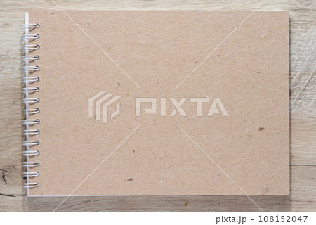Spiral notepad on a wooden table. The notebook has a rectangular shape and a cover made of craft paper. 108152047