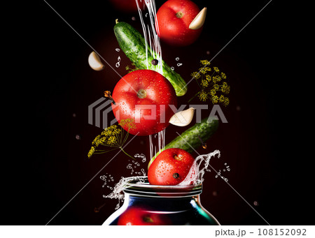 Canned tomatoes and cucumber in glass. Black background, horizontal. Food levitation, tomatoes, garlic, peppers and dill in the air. Canning, fermentation, pickles Canned tomatoes and cucumber in glass. Black background, horizontal. Food levitation, tomatoes, garlic, peppers and dill in the air. Canning, fermentation, pickles 108152092