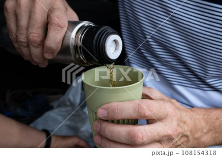 Male hands pour coffee or tea from a thermos into a reusable glass. Zero waste concept, outdoor recreation Male hands pour coffee or tea from a thermos into a reusable glass. Zero waste concept, outdoor recreation 108154318