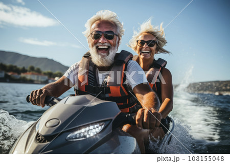 Happy senior couple in safety helmets and vests riding jet ski on a lake or along sea coast. Active elderly people having fun on water scooter. Retired persons lead active lifestyle and travel. 108155048