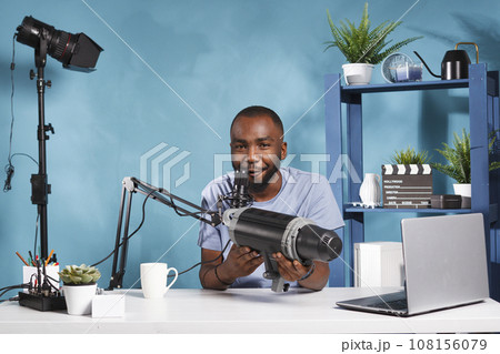 African american videographer reviewing studio professional lightning equipment on technology online blog. Young vlogger holding photography gear and recording product presentation video African american videographer reviewing studio professional lightning equipment on technology online blog. Young vlogger holding photography gear and recording product presentation video 108156079