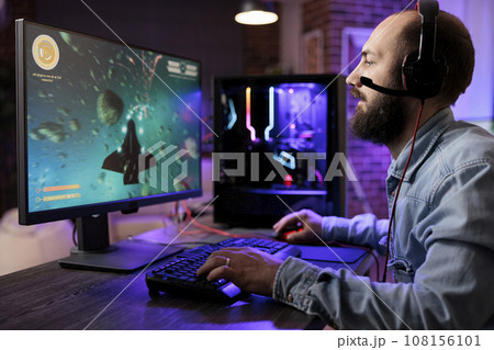 Gamer playing classic arcade action space videogame, shooting meteorites using lazer beams. Man enjoying leisure time at home using high tech gaming PC to solve missions in singleplayer game 108156101