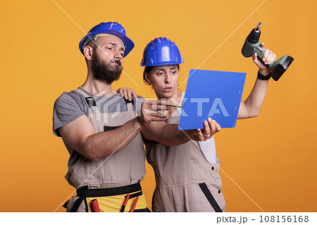 Team of construction workers analyzing papers on clipboard, taking notes of measurements. Builders looking at files with building or renovating information, engineering skills with power drill. Team of construction workers analyzing papers on clipboard, taking notes of measurements. Builders looking at files with building or renovating information, engineering skills with power drill. 108156168