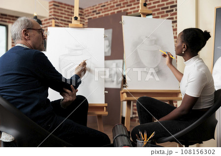 Diverse different aged people students talking during drawing class, senior man and young woman communicating during art course, improving sketching skill. Creative hobbies for adults Diverse different aged people students talking during drawing class, senior man and young woman communicating during art course, improving sketching skill. Creative hobbies for adults 108156302
