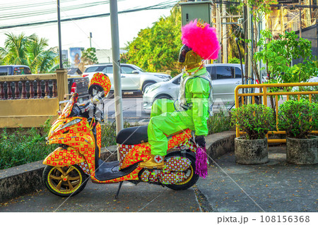 Robot in pink wig, golden crown, green suit sitting on painted scooter on city street Robot in pink wig, golden crown, green suit sitting on painted scooter on city street 108156368