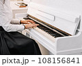 Beautiful woman dressed in white dress playing on white piano 108156841
