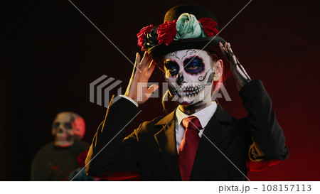 Spooky female model wearing santa muerte costume in studio, having black and white skull make up. Celebrating day of the dead holy mexican tradition, festival body art horror look. Handheld shot. Spooky female model wearing santa muerte costume in studio, having black and white skull make up. Celebrating day of the dead holy mexican tradition, festival body art horror look. Handheld shot. 108157113