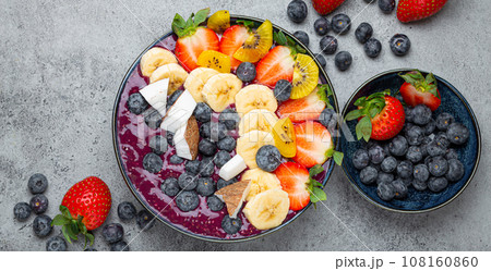 Healthy summer acai smoothie bowl with chia seeds, fresh banana, strawberry, blueberry, cocos, kiwi top view, rustic concrete background with spoon Healthy summer acai smoothie bowl with chia seeds, fresh banana, strawberry, blueberry, cocos, kiwi top view, rustic concrete background with spoon 108160860