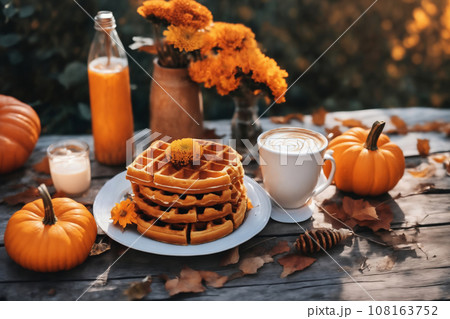 still life of a cup of hot latte and waffers and pumpkins on an old wooden table against the background of beautiful autumn nature at sunset, decoration for Halloween 108163752