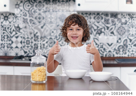 Happy boy feels happiness while eating healthy breakfast of cornflakes and milk at the kitchen. 108164944