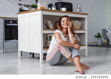 Cute girl sitting on the floor on the background of stylish kitchen. Womens housework concept. 108164998
