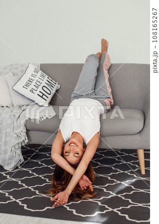 Beautiful woman relaxing on a grey couch with head upside down. Cute girl having fun at cozy home in lazy day. Beautiful woman relaxing on a grey couch with head upside down. Cute girl having fun at cozy home in lazy day. 108165267