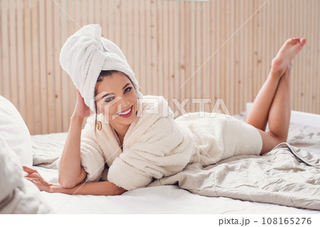 A beautiful happy young woman lies on the bed at home with white cover magazine near her. Beautiful girl enjoying on the bed in morning. 108165276