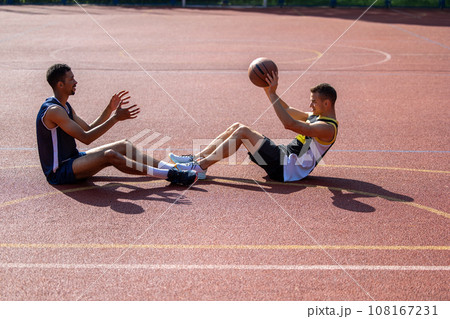 Men basketball players sitting together on court throwing ball to each other. 108167231